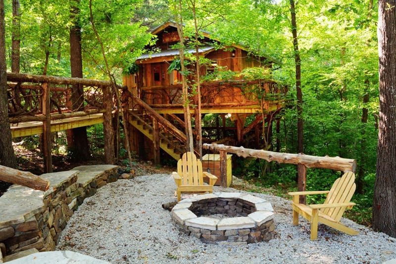 view of treehouse glamping Arkansas with firepit and bridge to wooden treehouse in the forest