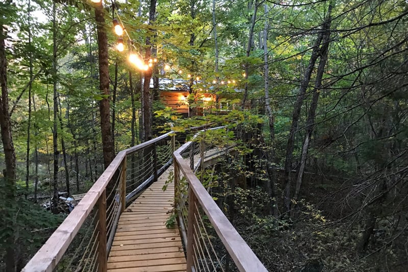 Ash Hill Treehouse in the Adirondacks view from the bridge to the treehouse with lights above and treehouse surrounded by trees