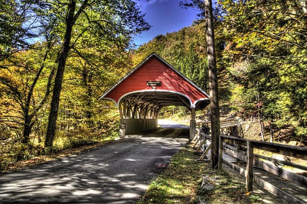 covered red bridge in Vermont with trees around it. 