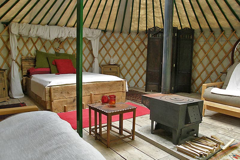 Cae Wennol Luxury Yurts North Wales view of inside with bed, stove, couch and table