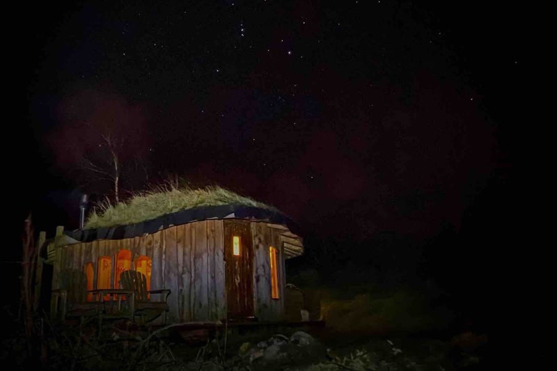 Cosy Wooden Fairy House view of yurt at night with yurt having grass on roof