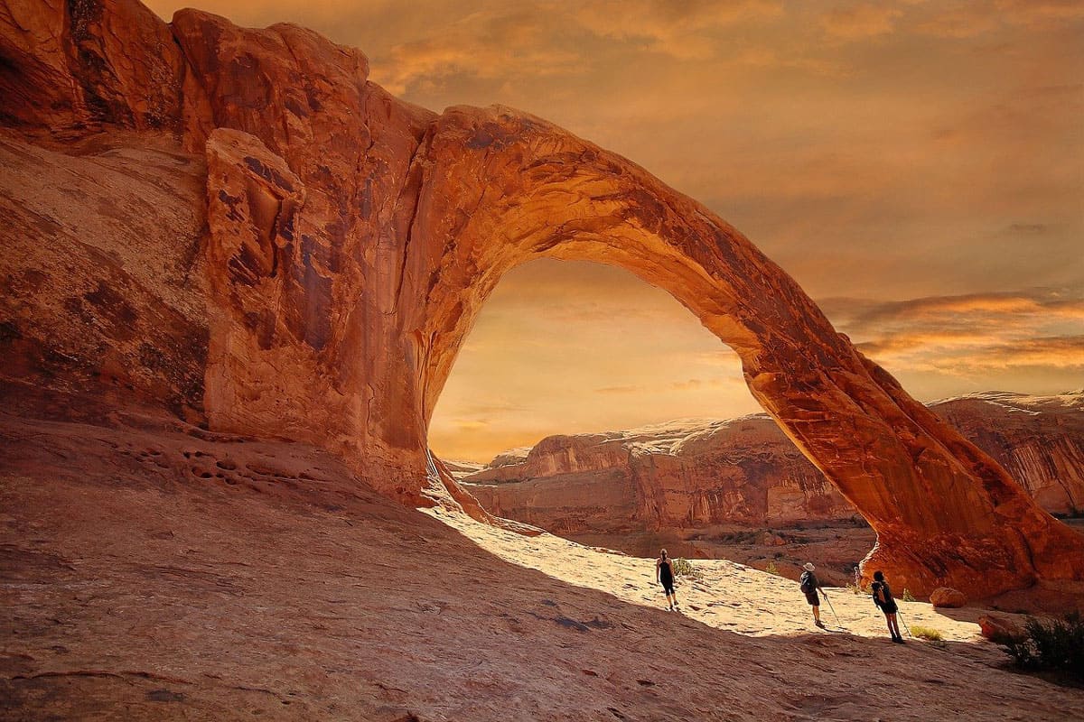 Utah glamping in moab view of an arch with hikers looking at it during sunset