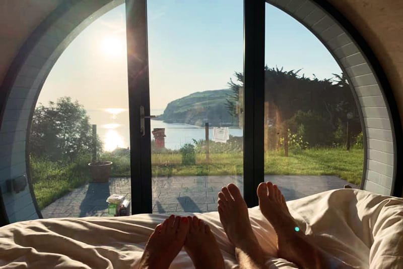 Glenarm Castle Pod Glamping view from the pod bed through the window with feet on bed and view of the coast
