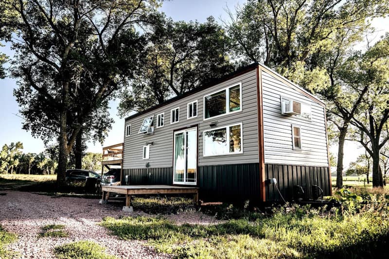 Gorgeous Tiny House Glamping in Nebraska view of grey tiny home with lots of windows and trees around