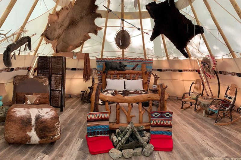 Lakota Luxury Tipi Arkansas Glamping view of inside of tipi with native decorations and log bed and animal skins on furniture