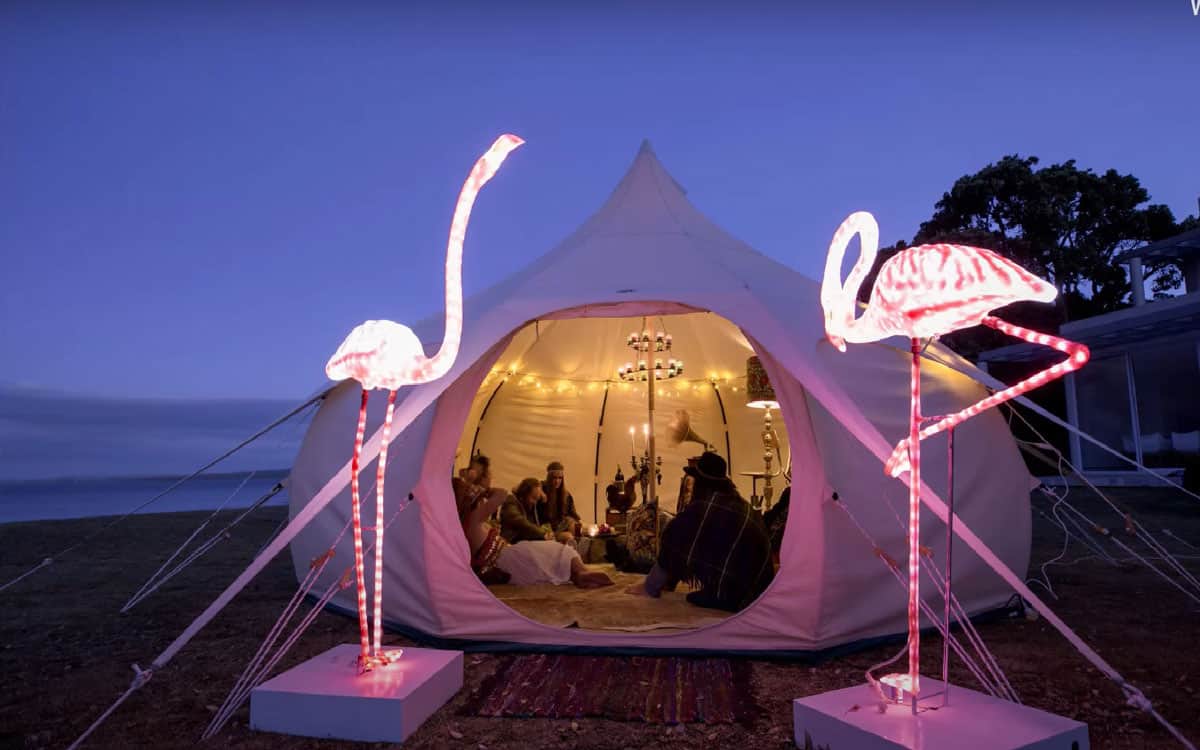 Lotus Belle Glamping Tents Sale view of tent in the dark with two flamingo lights and people lounging in the tent. 