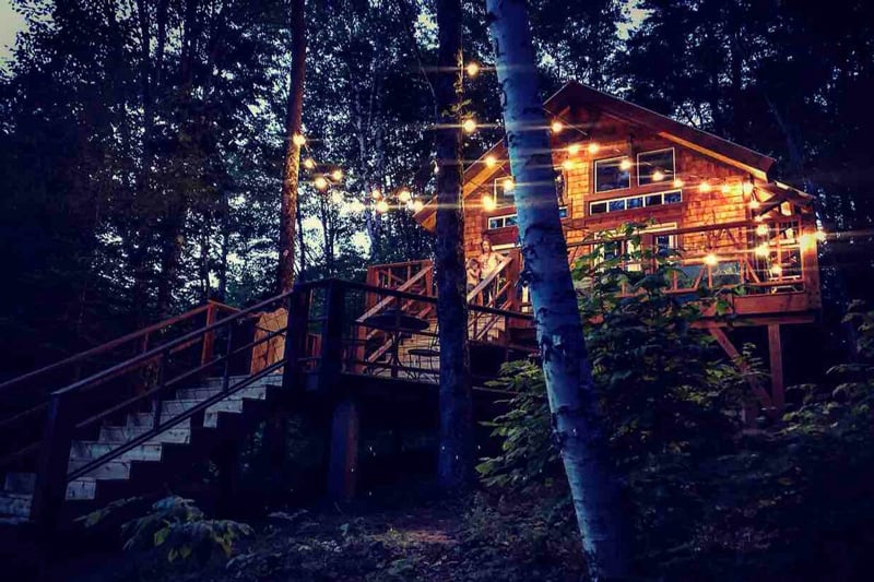 Luxury Vermont Treehouse Dog Mountain view at night with stairs and lights strung above deck