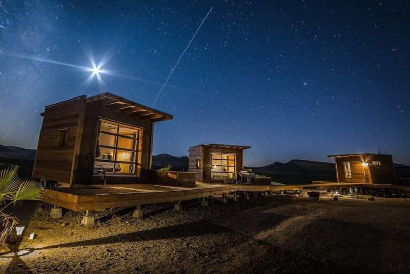 Mojave Desert Eco-Pods view of the pods and bathroom at night with wooden walkway between them