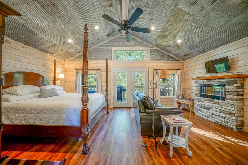 Mountain Air Treehouse Glamping in Arkansas view of inside with poster bed, couch, wood floors and deck outside