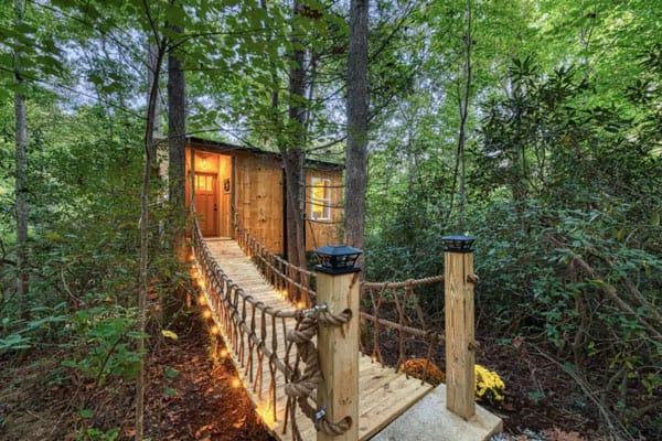 Romantic Asheville Treehouse with Hot Tub view from bridge with lights on and trees around it