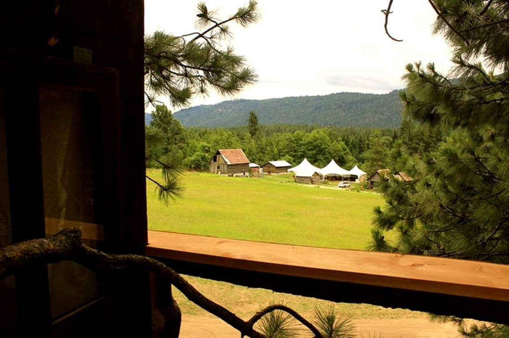 treehouse Glamping in Washington State with view off the deck onto the grass field and a barn and tents in the background
