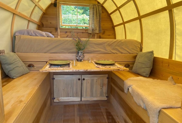 inside of the sheepherder glamping wagon with a bed and table and seats. 