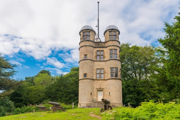 Glamping Peak District hunting tower with cannons on the ground in front and trees around it.