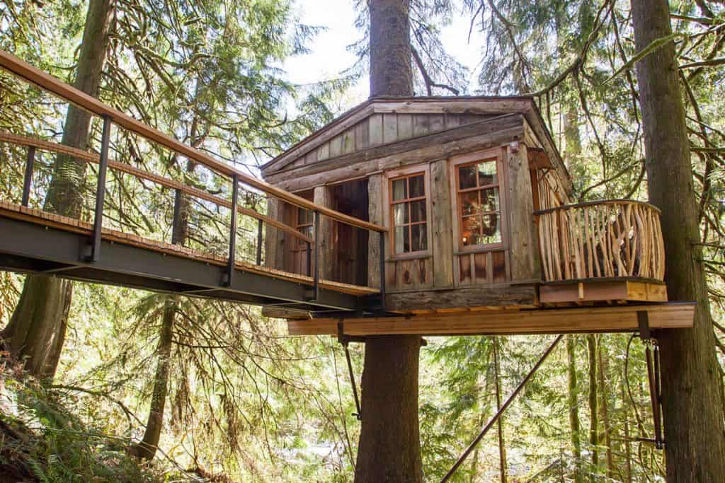 treehouse point Glamping in Washington State view of treehouse in trees with bridge going to it