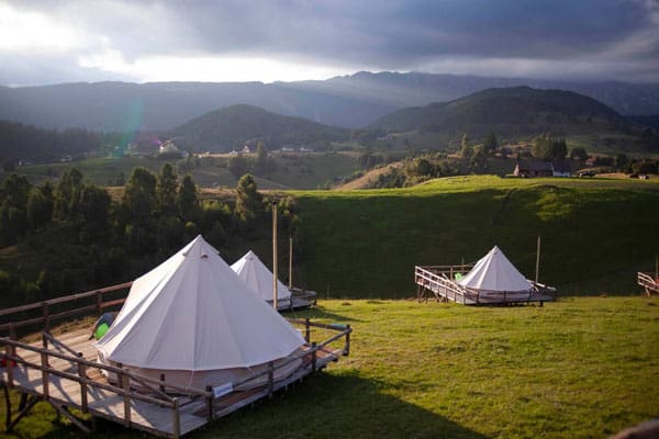 Ursa Mica Glamping Resort Romania view of multiple glamping tents on the grassy hill with the mountains in the distance