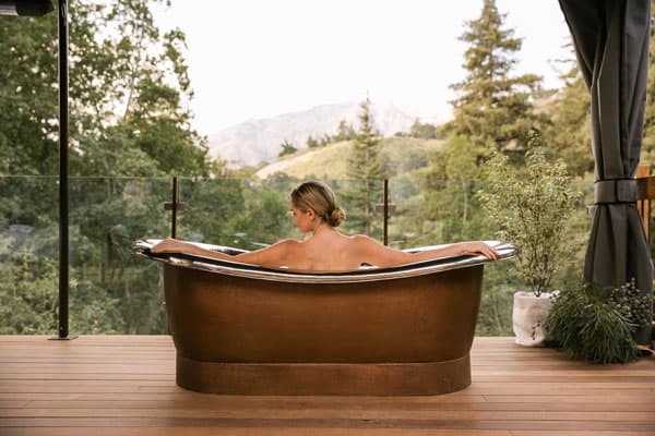 Ventana Big Sur Glamping Resort copper tub with view of the area, woman sitting in tub with arms spread