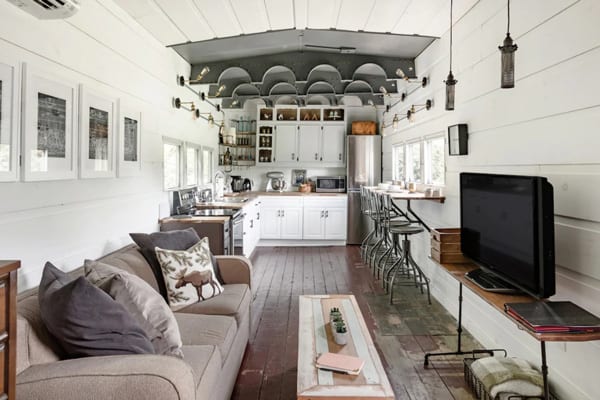 Converted WWII glamping Train Car with Patio inside view with tv, couch, kitchen and wood floors and white walls